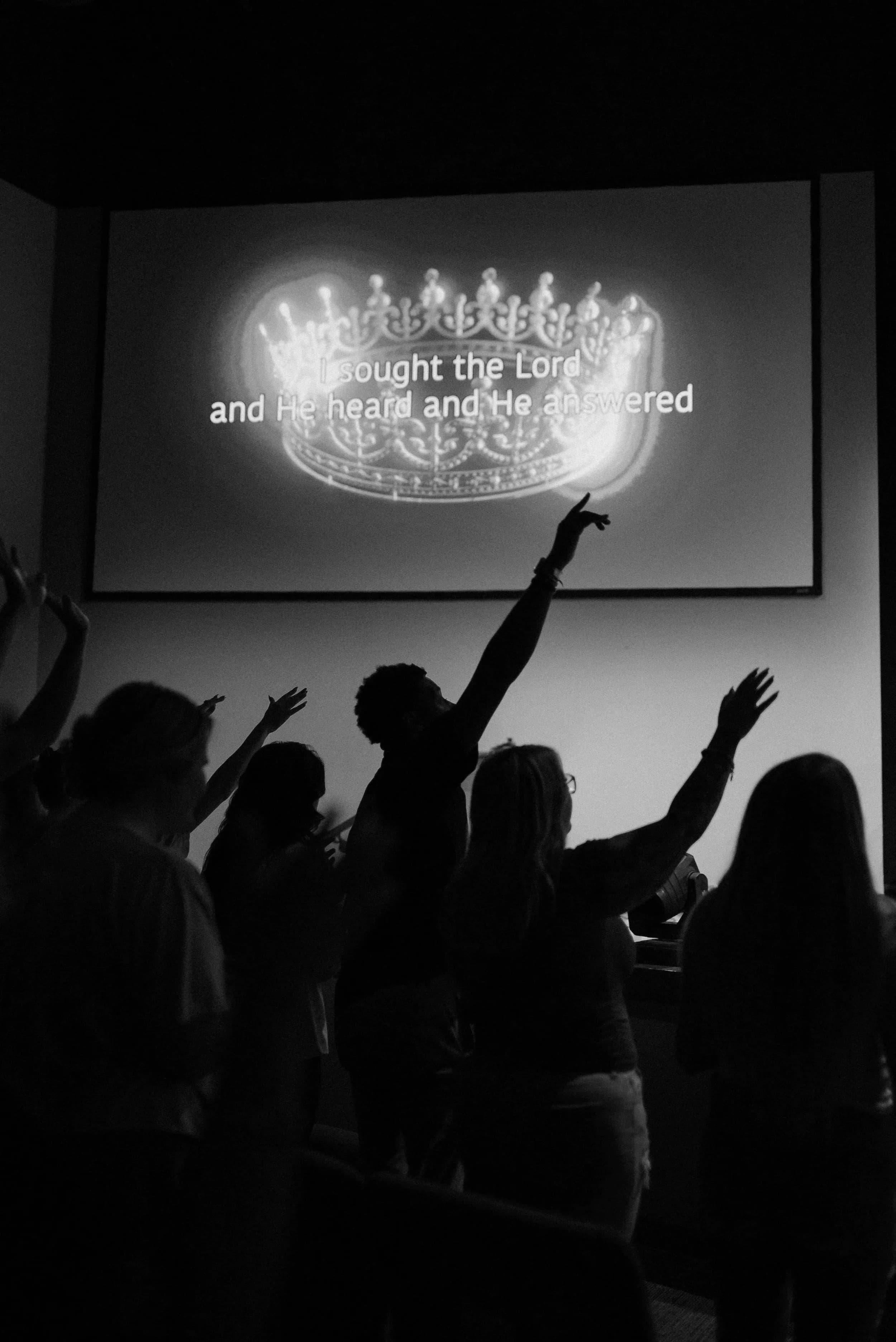 Hands raised in worship beneath lyrics on a screen