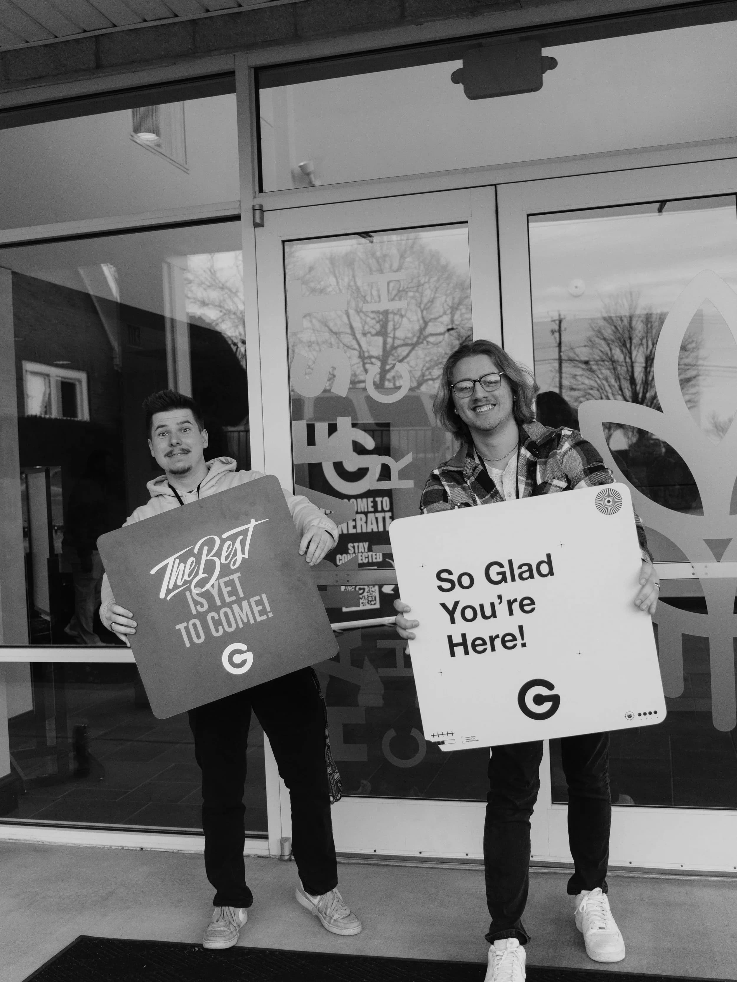 Two volunteers welcoming people at the door with signs